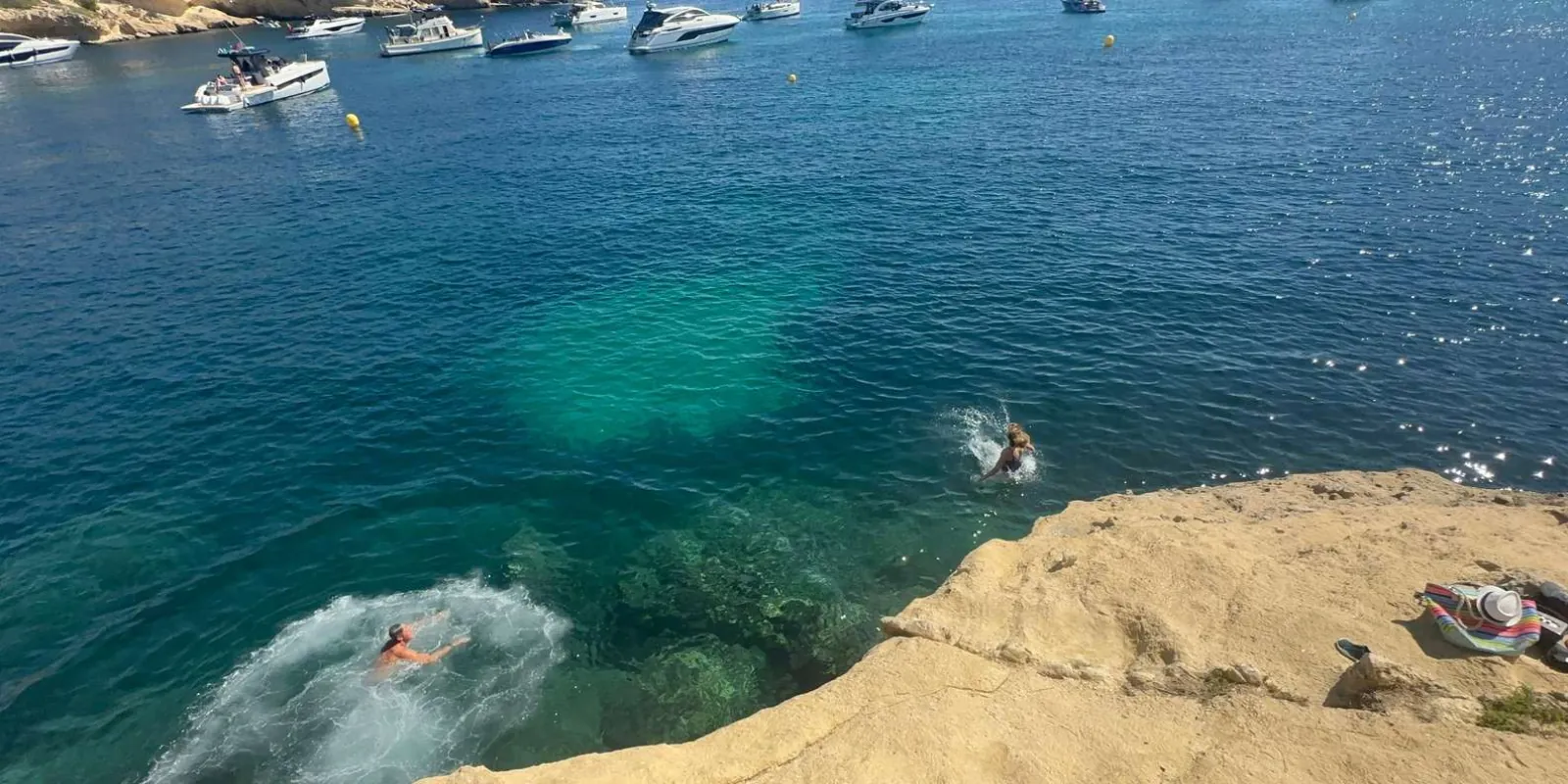 Cliff jumping at a Mallorca cove with snorkellers visible in the clear green water below