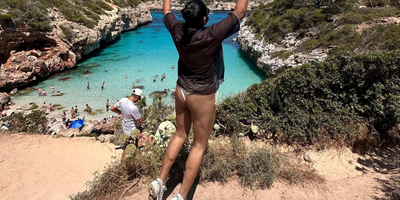 Tour guest jumping with arms raised overlooking the turquoise cove of Caló des Moro — Mallorca