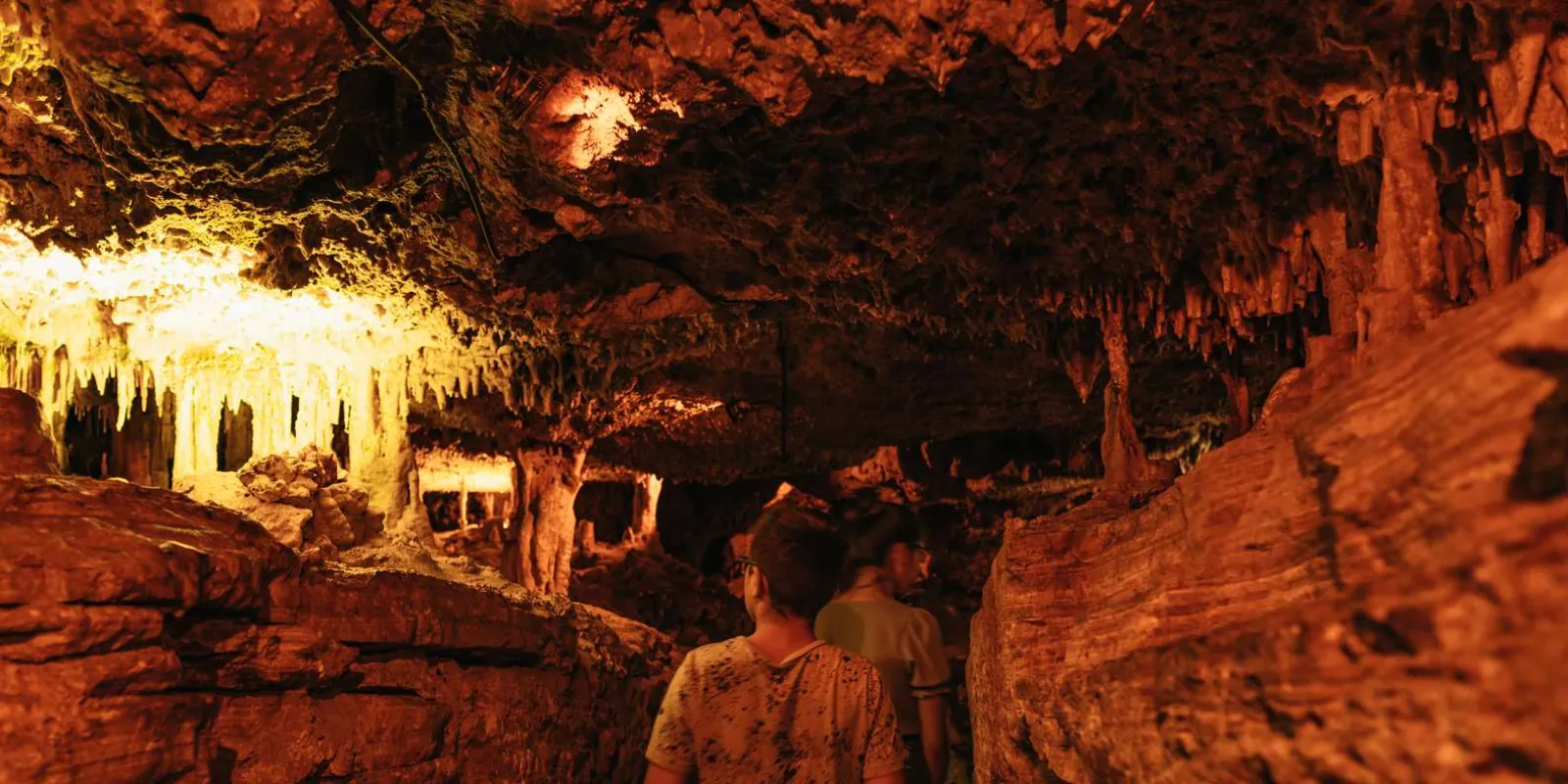 Caves of Hams visitors admiring hanging stalactite curtains under amber cave lighting — Mallorca