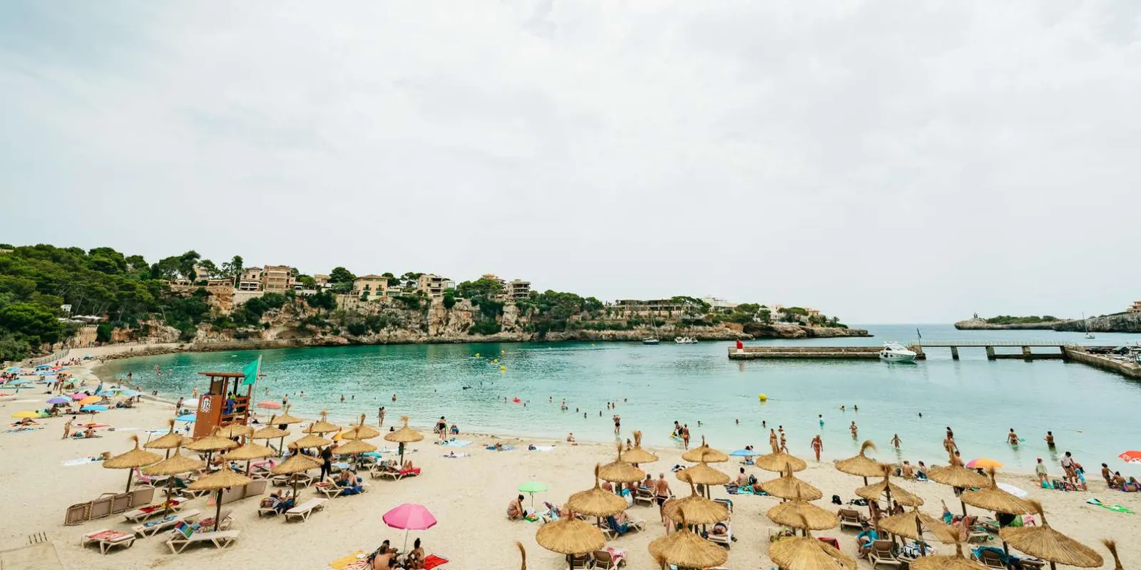 Porto Cristo beach with straw umbrellas, sunbathers and the calm natural harbour in view — Mallorca