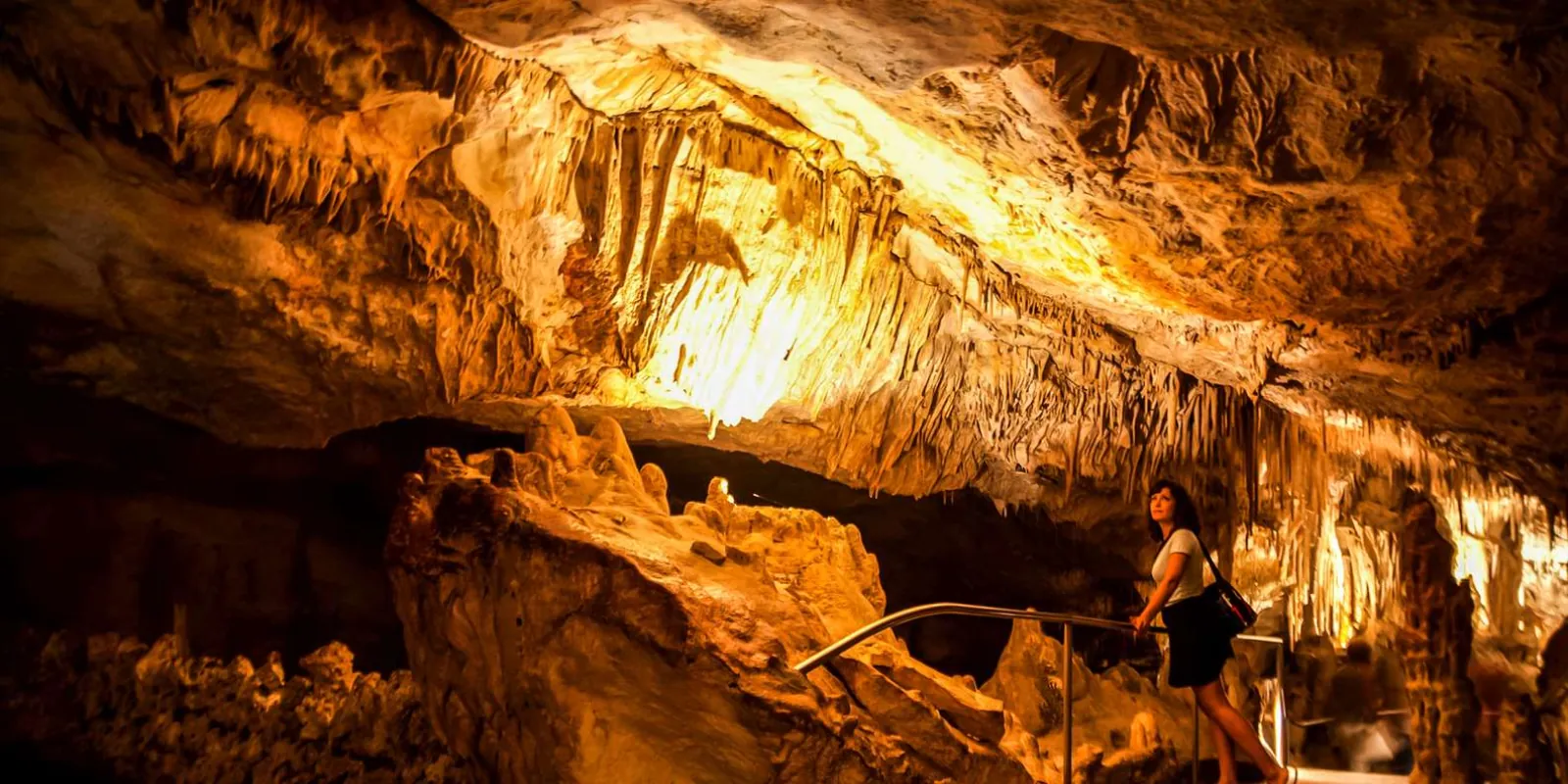 Caves of Drach illuminated chamber with towering rock formations and a visitor on the handrailed path — Mallorca