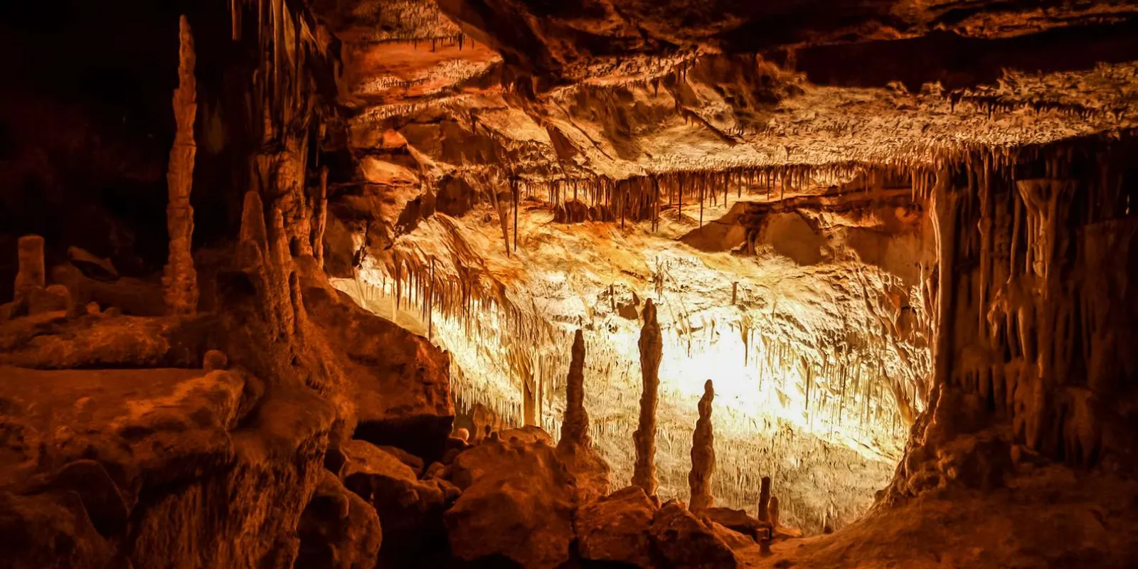 Caves of Drach deep chamber with dramatic stalagmite pillars and orange cave lighting — Mallorca