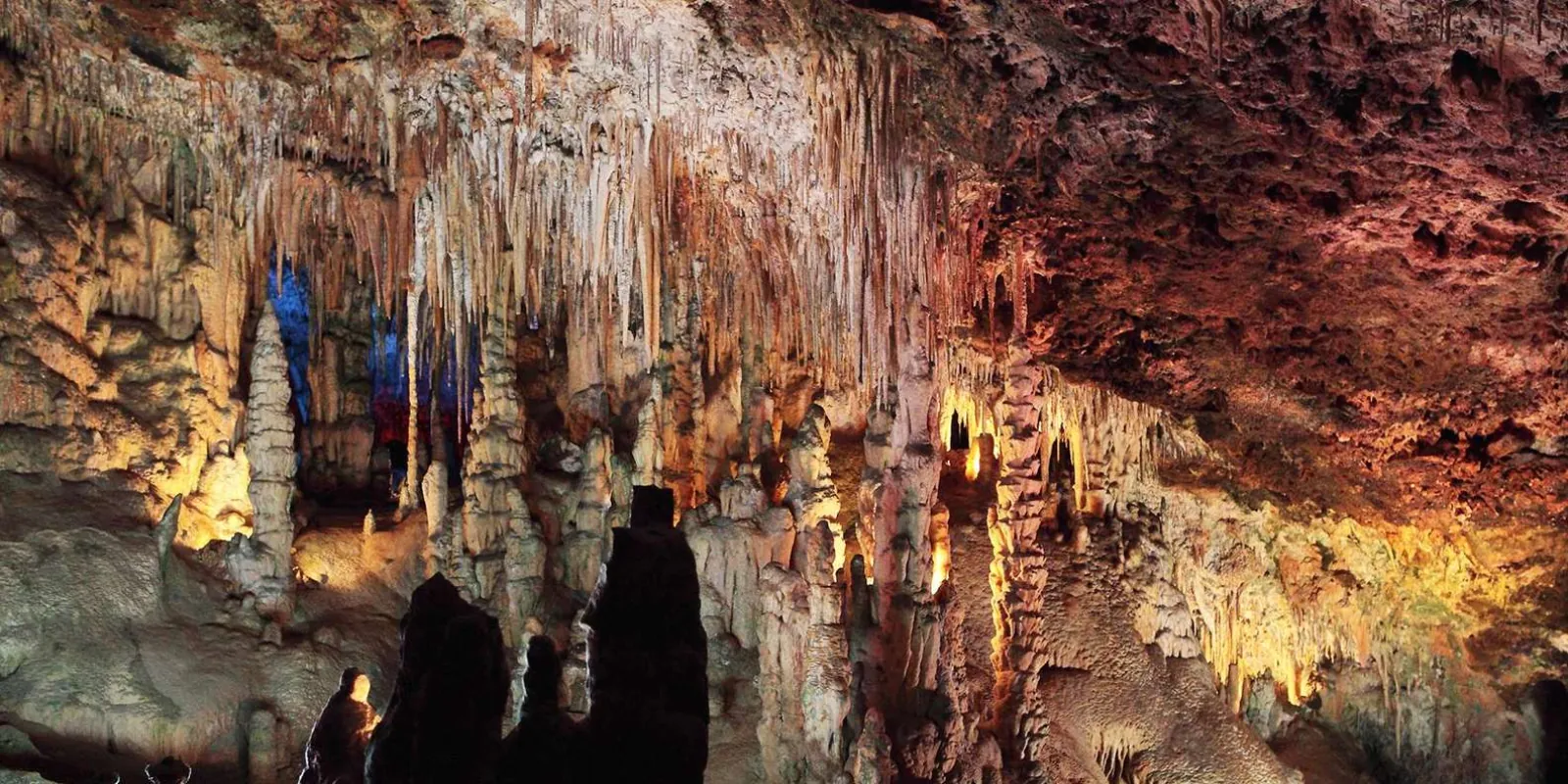 Caves of Drach illuminated chamber with white and amber stalactites and coloured accent lighting — Mallorca