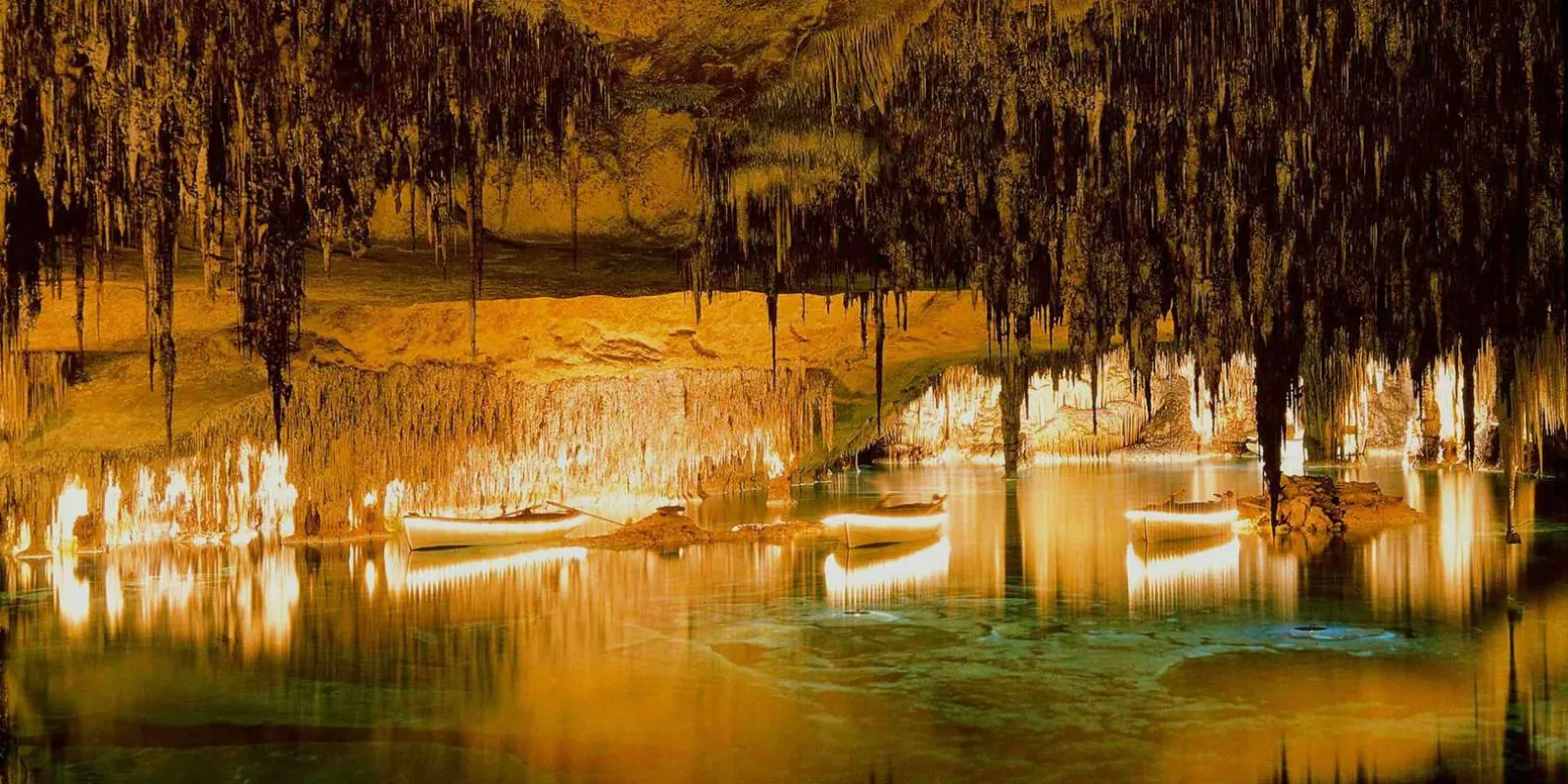 Caves of Drach Lake Martel with wooden boats moored under dense dark stalactite canopy — Mallorca